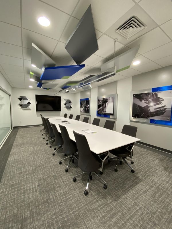 Conference room with a long white table, gray task chairs and suspended blue and gray acoustic panels